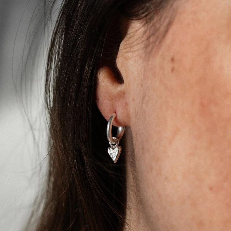 Close-up of an ear wearing a silver hoop earring with a heart charm.