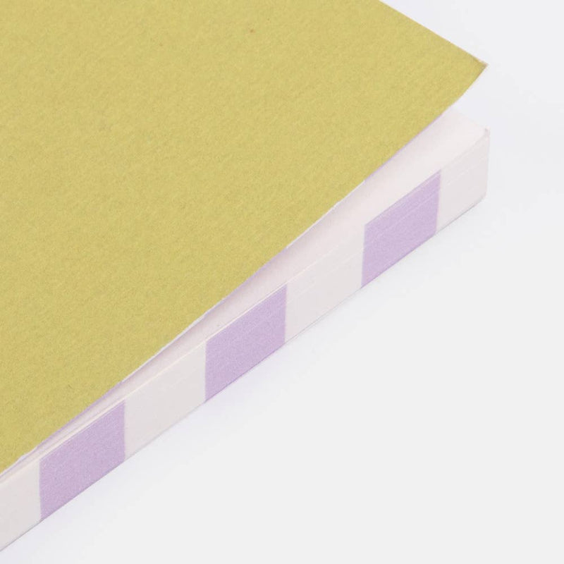 Close-up of a book with a textured yellowish cover and purple square stickers on a white background
