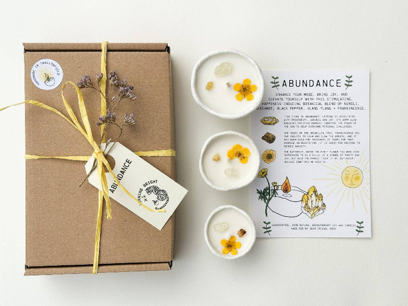 Gift box with a yellow ribbon, three small white bowls with flowers, and an 'Abundance' card on a white background.