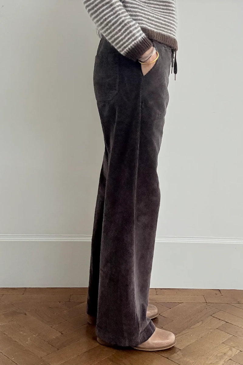 Person wearing dark gray wide-leg pants and a striped sweater against a plain wall.