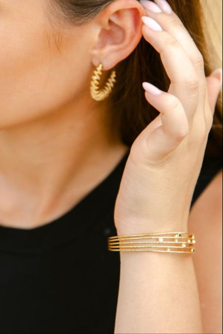 Woman wearing gold hoop earrings and bracelets, with a blurred background
