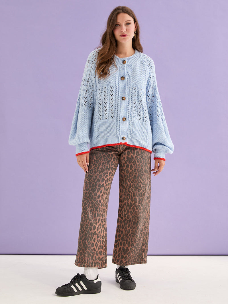 Woman wearing a light blue sweater with brown buttons and leopard print pants against a purple background