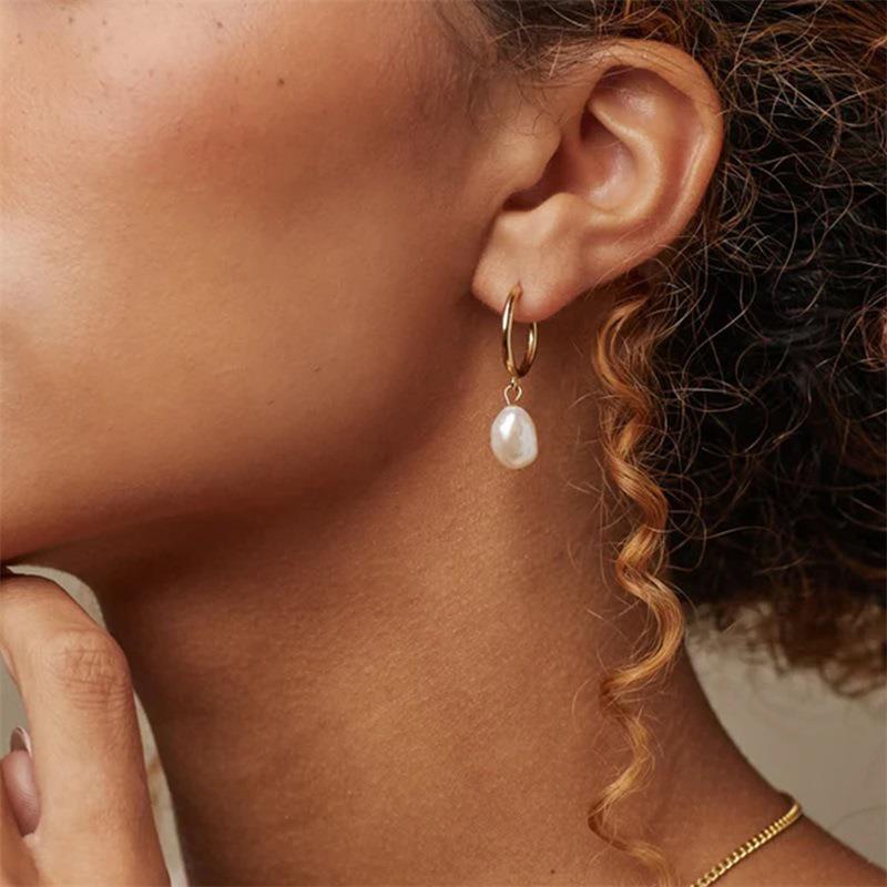 Close-up of an ear wearing a gold hoop earring with a pearl drop.