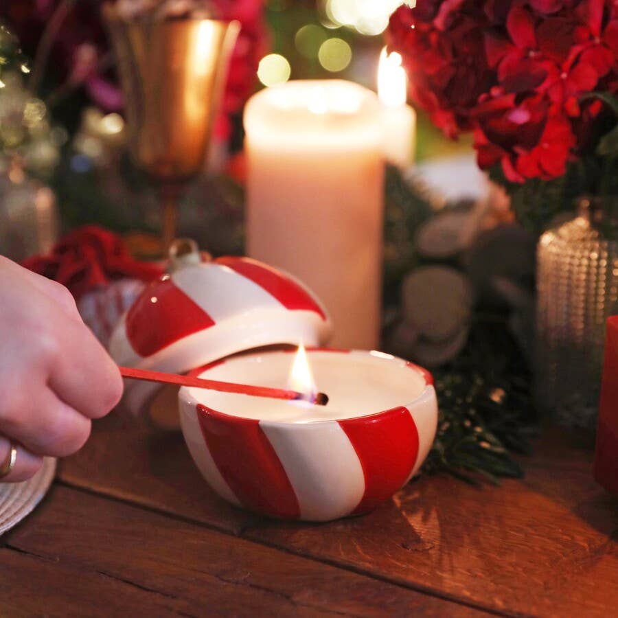 Person lighting a red and white striped candle with a festive background