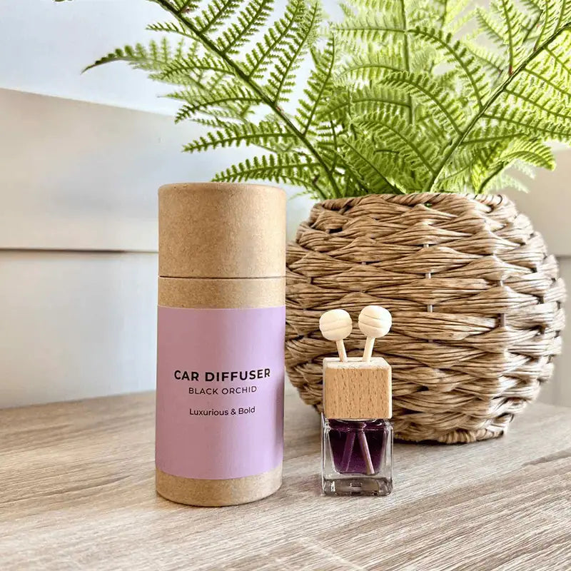 Car diffuser with cork lid and black orchid scent on a wooden surface with a plant in the background.