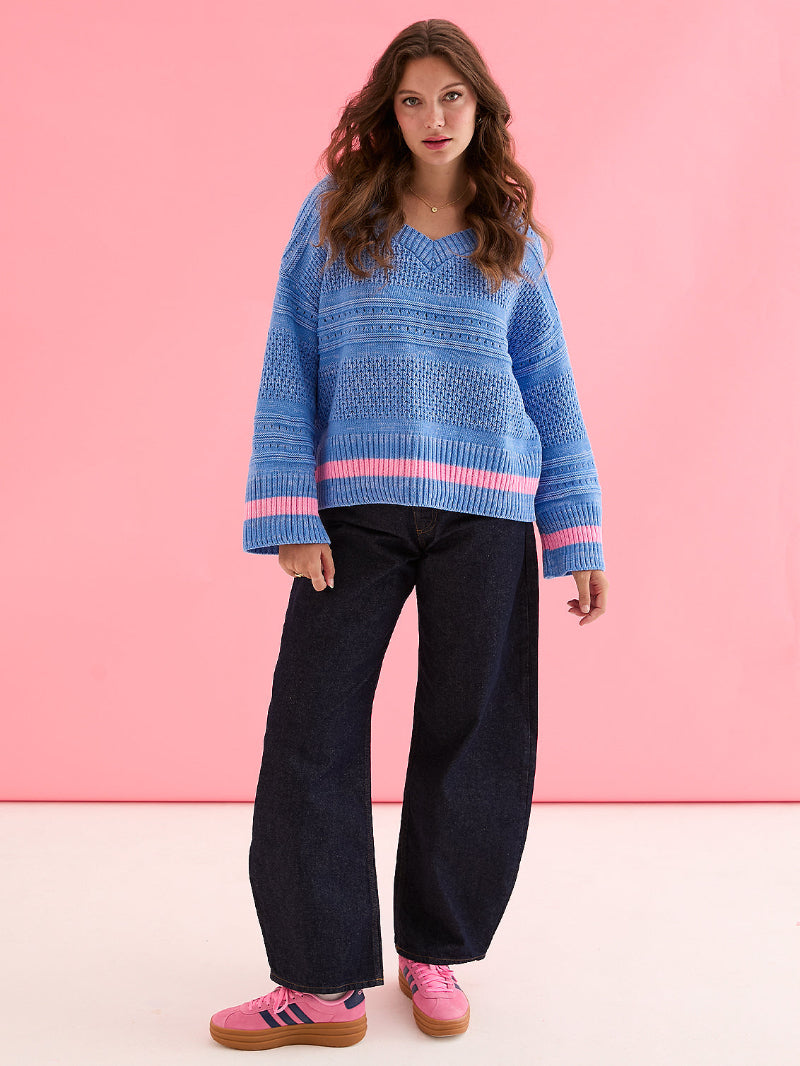 Woman wearing a Cara & The sky JudithJumper Blue_Front blue sweater with pink accents against a pink background