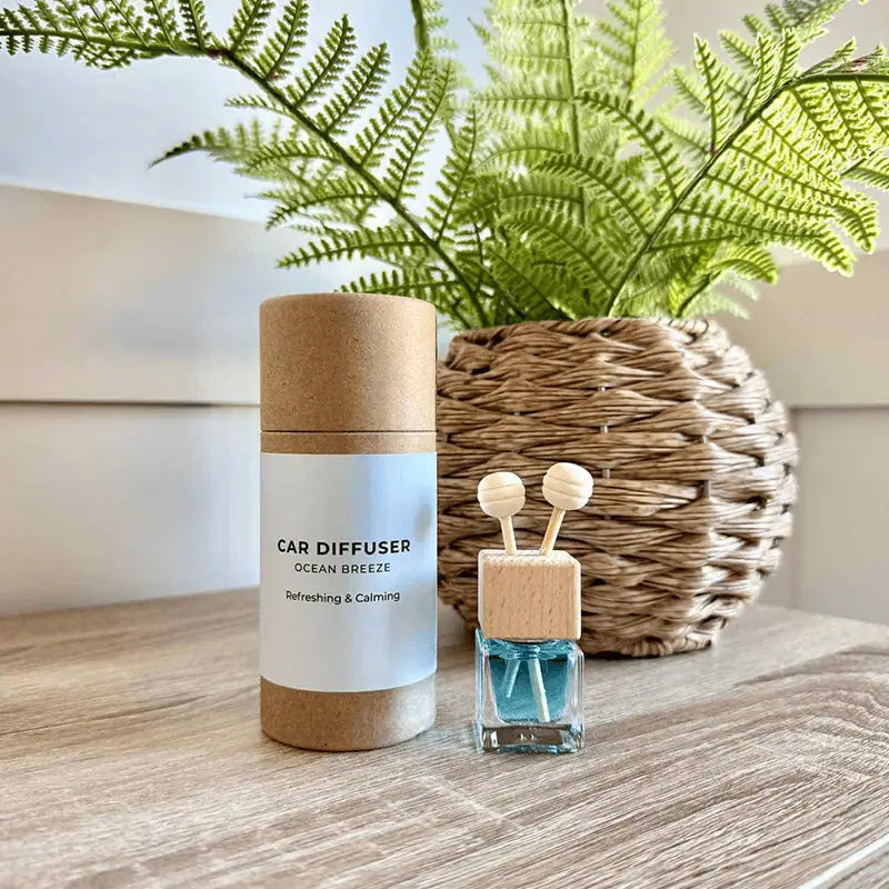 Car diffuser and small bottle with wooden sticks on a wooden surface with a plant in the background