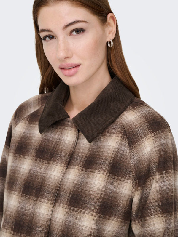 Woman wearing a brown and beige plaid coat with a plain background