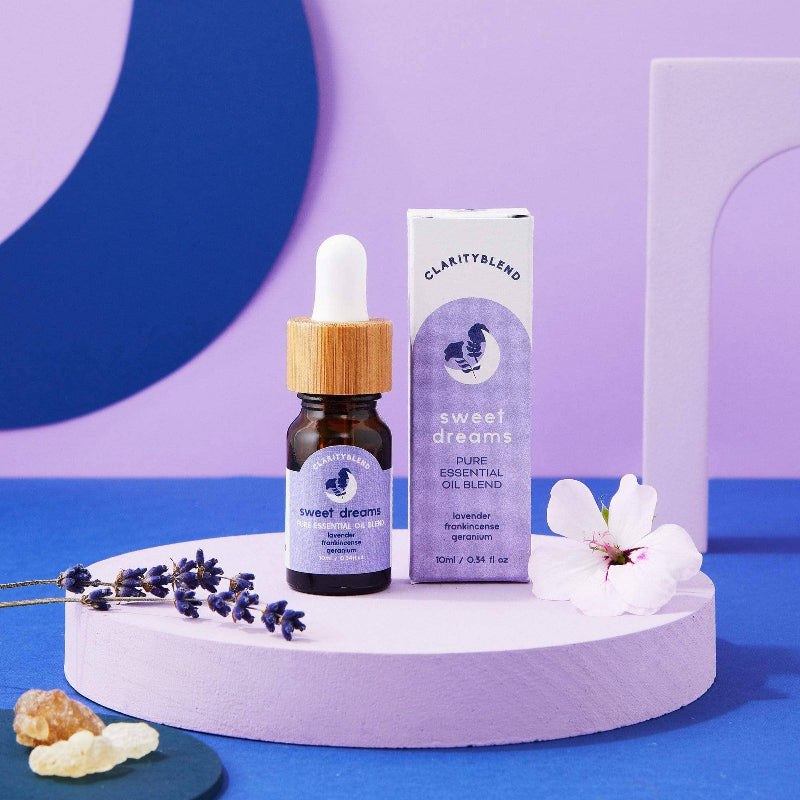 Bottle of 'Sweet Dreams' essential oil blend with dropper and packaging on a purple and blue background.