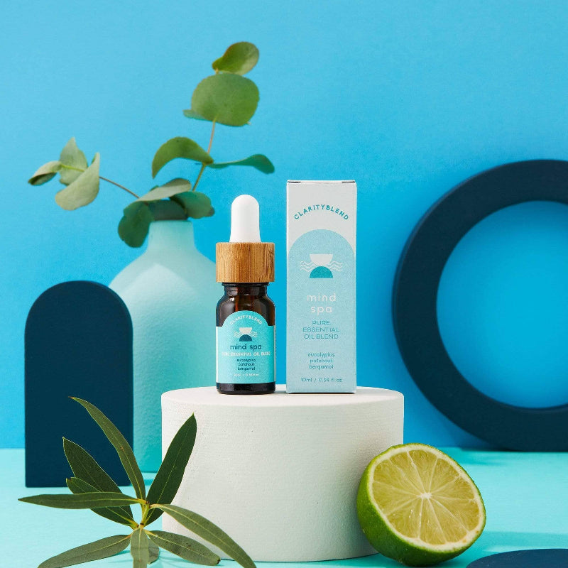 Bottle of essential oil with packaging on a white platform against a blue background