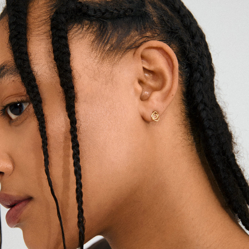 Close-up of a person wearing a gold earring with a white background