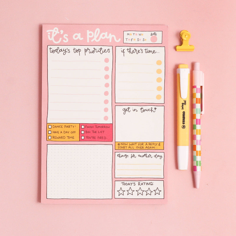 Note pad with planner stickers and two pens on a pink background