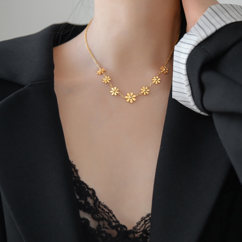 Gold floral necklace worn by a person in a black outfit with a gray sweater.