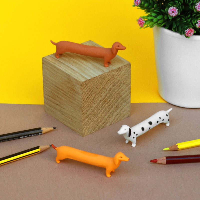 Dog-shaped erasers on a wooden block with pencils and a plant in the background.