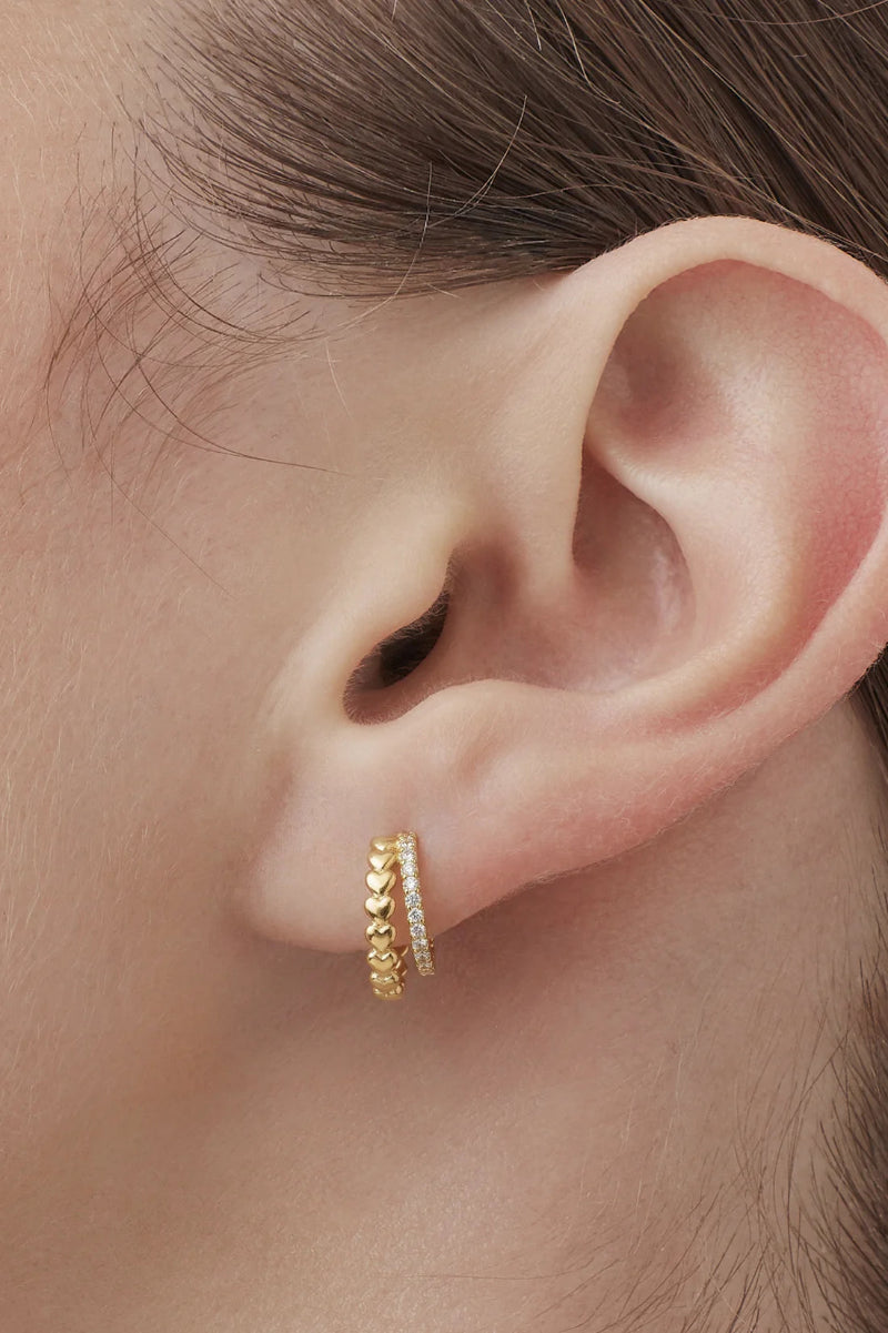 Gold hoop earring worn on an ear with a blurred background