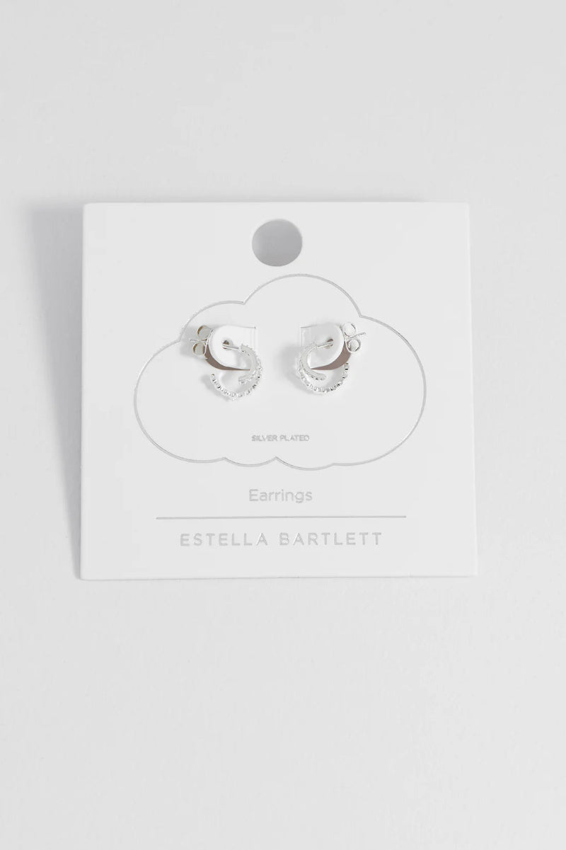 Silver earrings on a white card with 'Estella Bartlett' branding against a light gray background