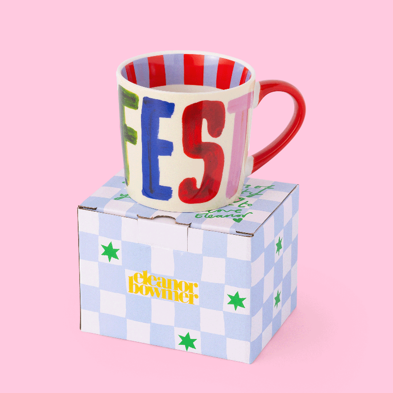 Colourful mug with 'MANIFEST' on a checkered box against a pink background