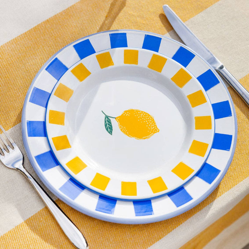 Decorative plate with lemon design and blue and yellow stripes on a yellow tablecloth.