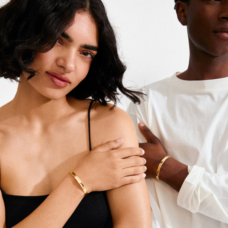 Two people embracing, one wearing a black dress and gold bracelet, the other in a white shirt.