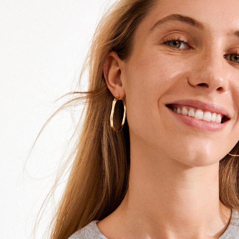 Close-up of a woman wearing gold hoop earrings with a plain background