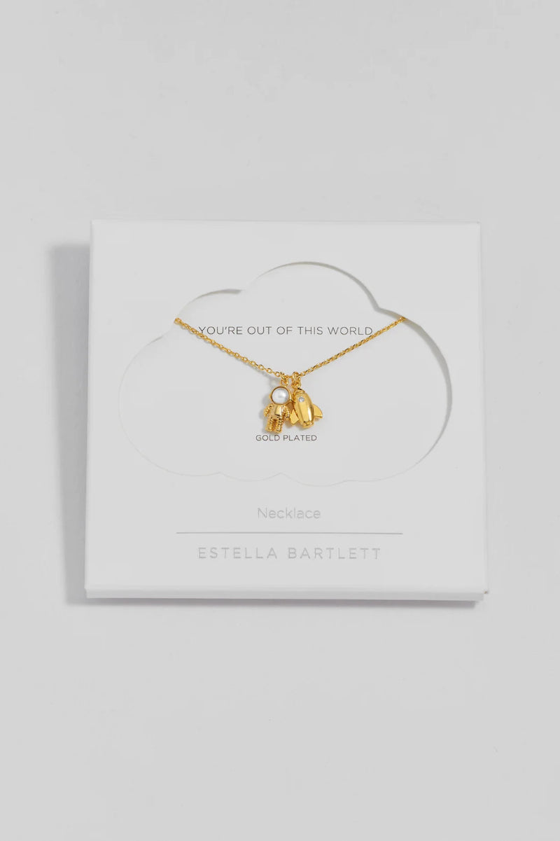 A gold-plated necklace with a small white pearl and two dangling gold charms, displayed on a white cloud-shaped backing card from Estella Bartlett.