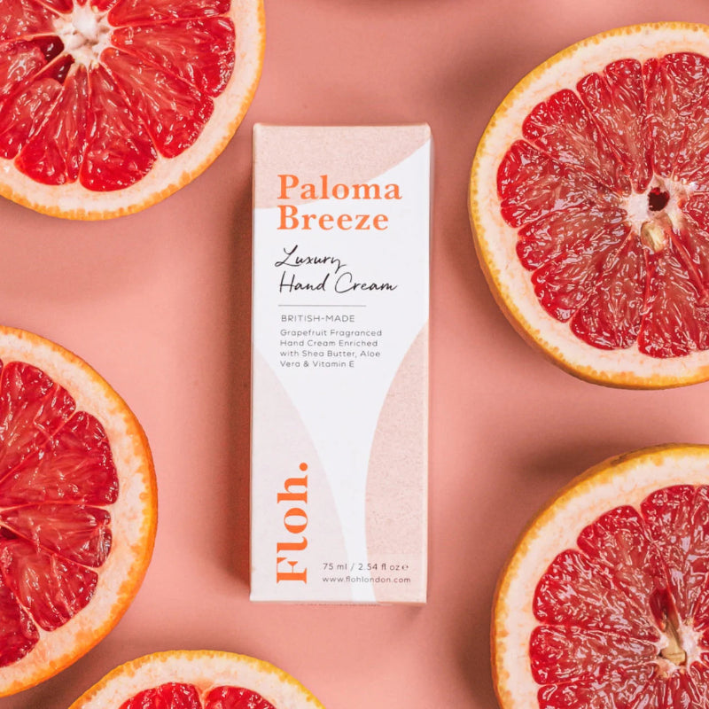 Paloma Breeze hand cream box surrounded by sliced grapefruits on a pink background
