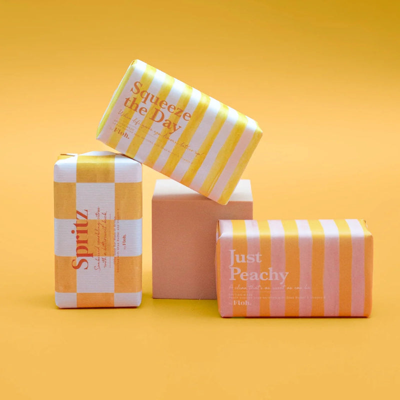 Four wrapped soap products with colorful packaging on a yellow background