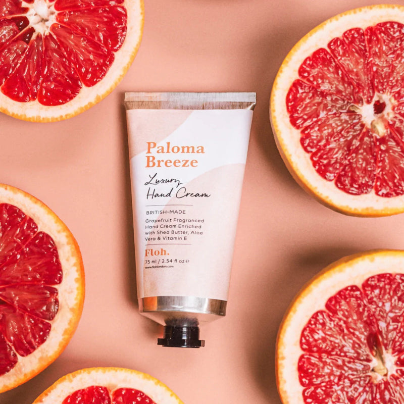 Paloma Breeze hand cream tube surrounded by sliced grapefruits on a peach background