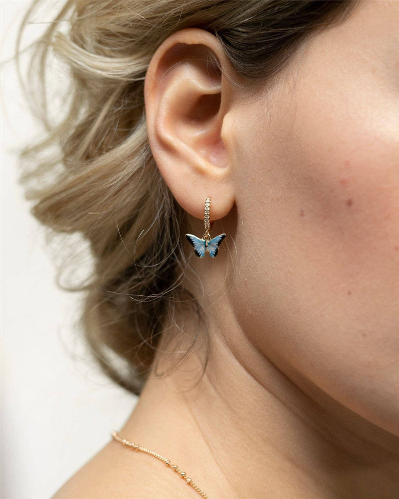 Close-up of a person wearing butterfly-shaped earrings with a blurred background