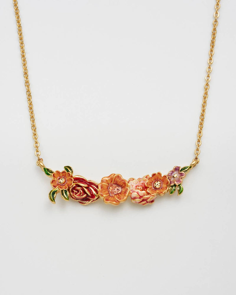 A gold chain necklace featuring a bar-shaped floral pendant with pink, red, and orange enamel flowers and green leaves, set against a plain light gray background.