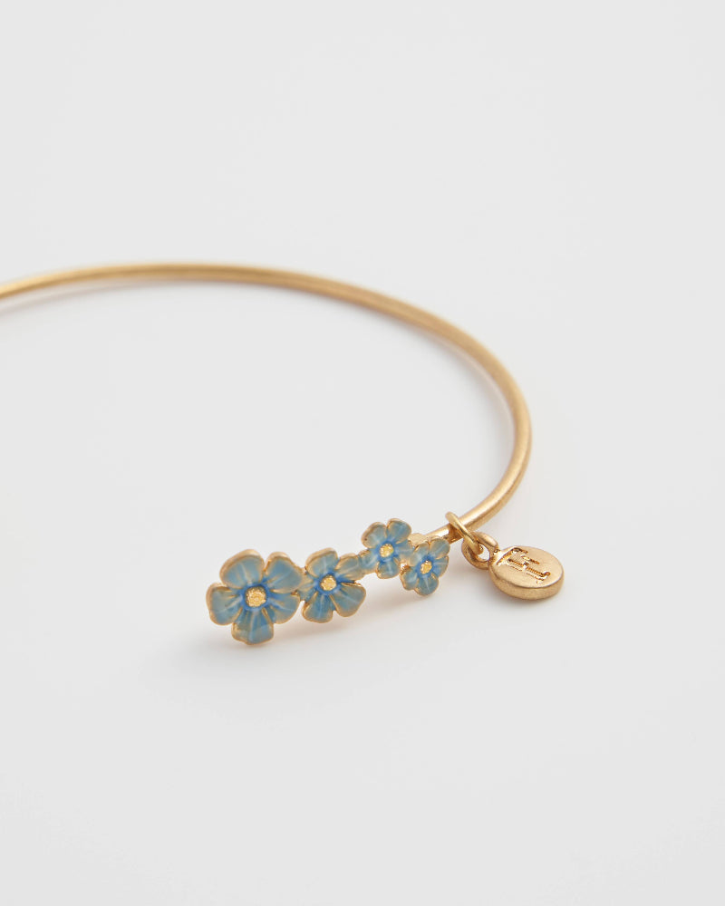 Fable Forget-Me-Not Bangle Gold bracelet with blue flower charms on a light gray background