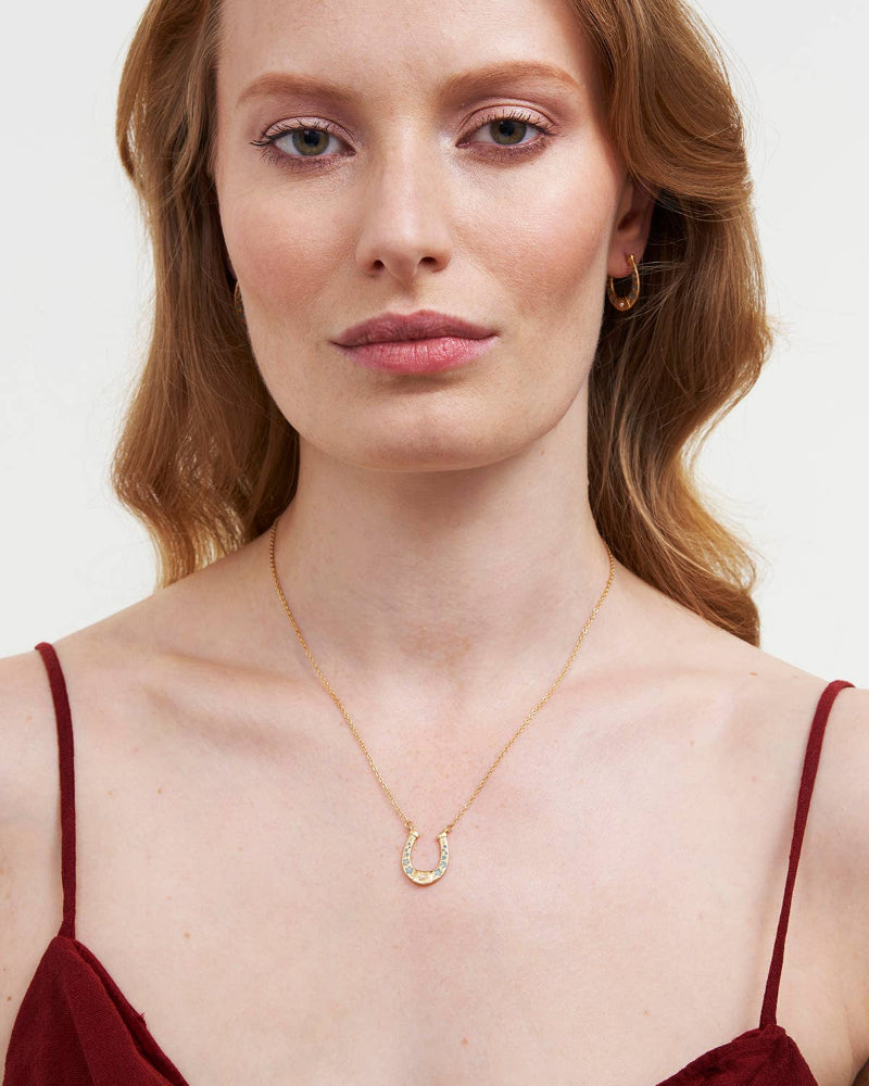 Woman wearing Fable Horseshoe Necklace with a horseshoe pendant on a plain background