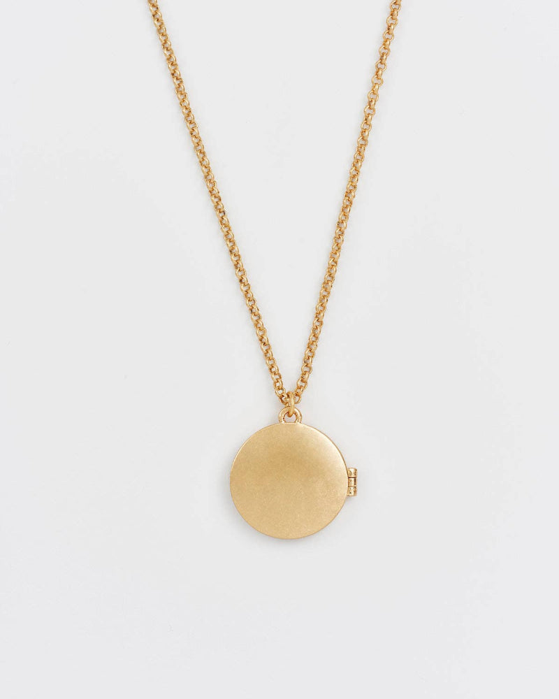 Gold necklace with a round pendant on a light grey background