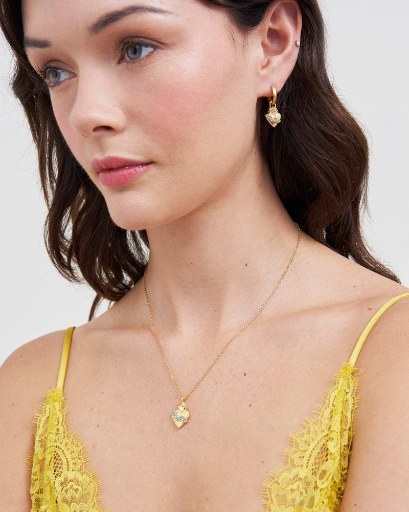 Woman wearing a Fable Sacred Heart Necklace and earrings against a white background