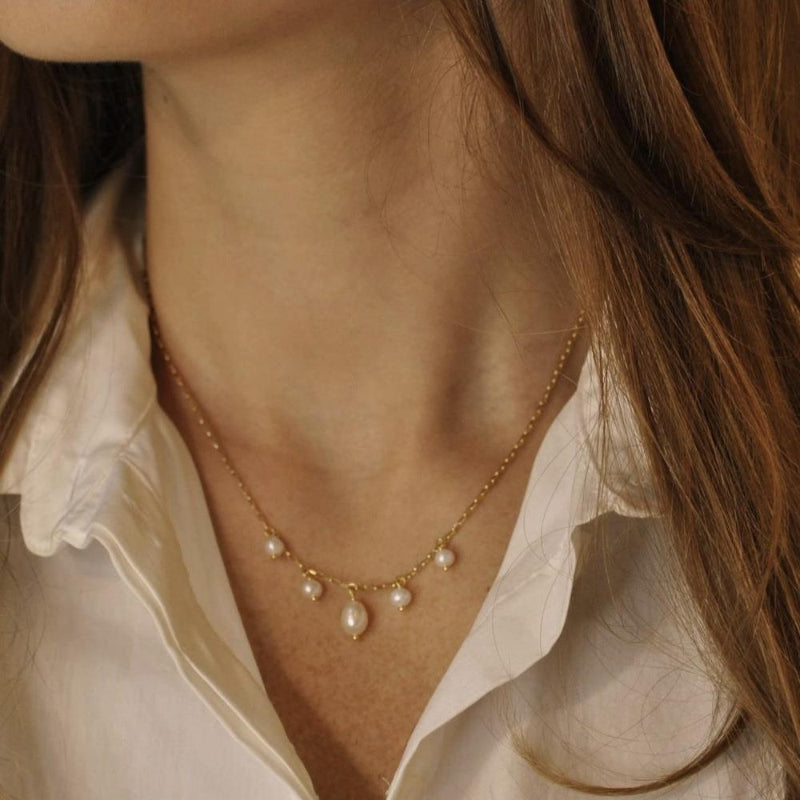 Close-up of a person wearing a delicate gold necklace with pearls.