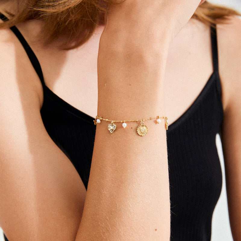 Gold bracelet with charms on a person wearing a black top.