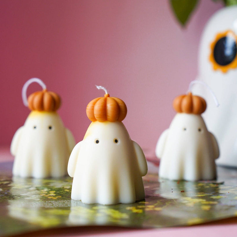 Candle-shaped ghost figures with pumpkin hats on a pink background