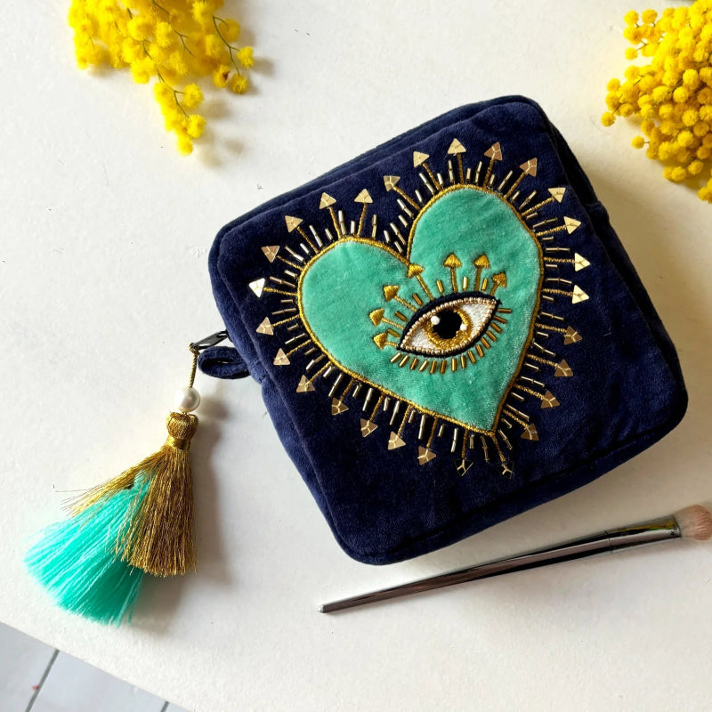 Navy blue pouch with green heart and eye design, tassel, and crochet hook on a white background with yellow flowers.