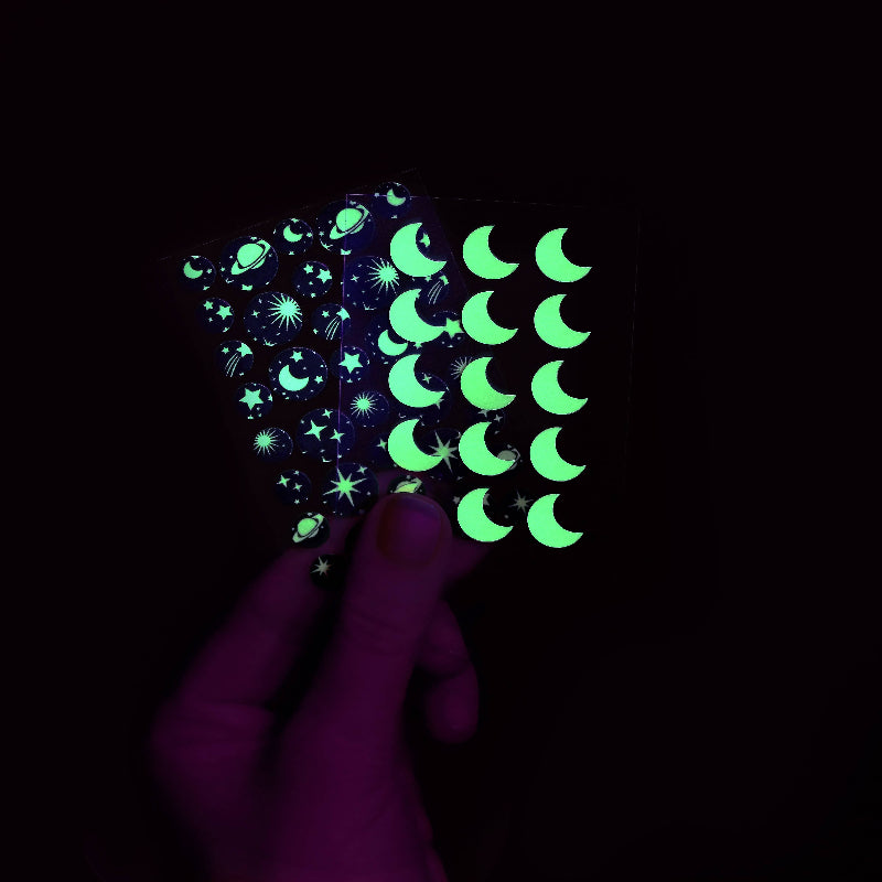 Glowing stickers with celestial designs held against a dark background
