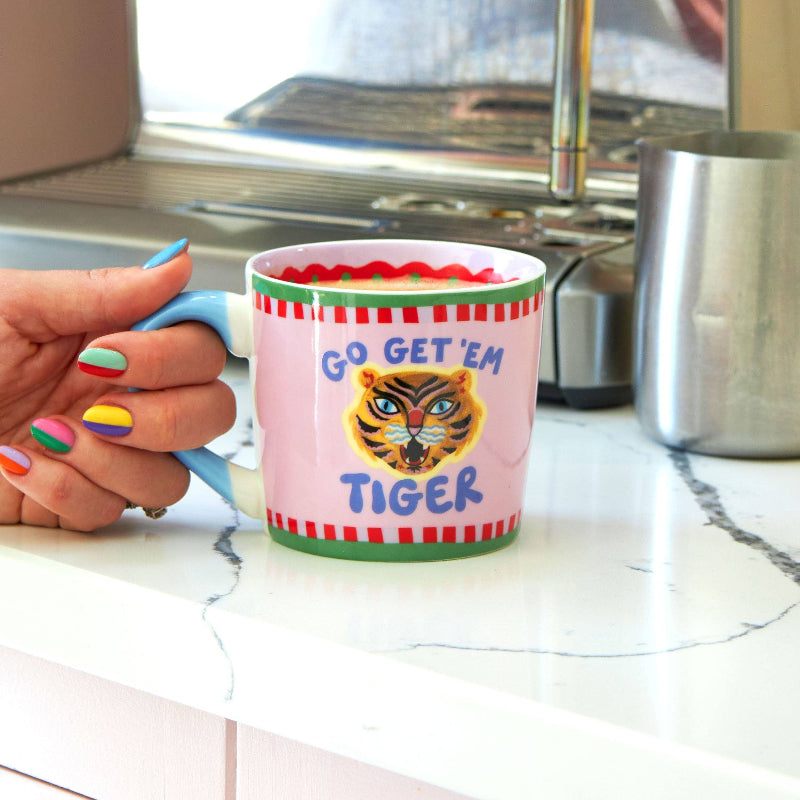 Person holding a mug with a tiger design and 'Go Get 'Em Tiger' text in a kitchen.