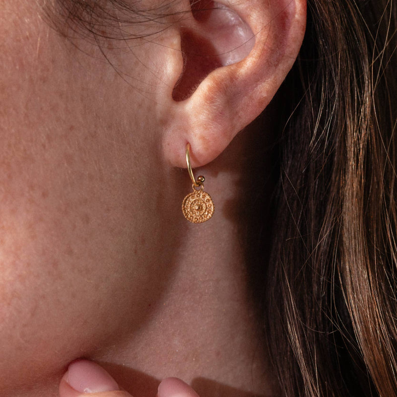 Close-up of a person wearing a gold earring with a circular design.