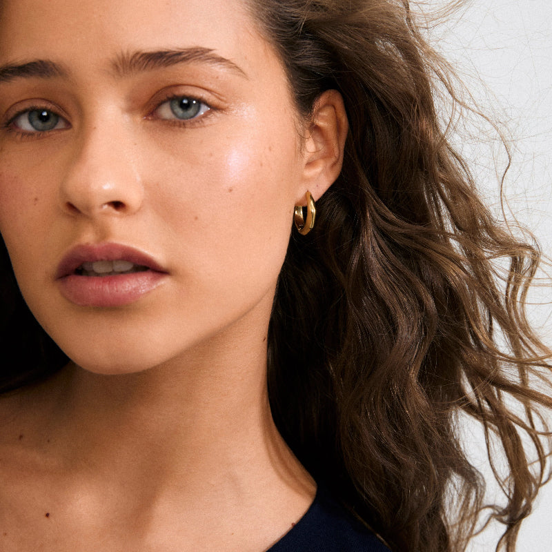 Close-up of a woman wearing gold hoop earrings with a neutral background