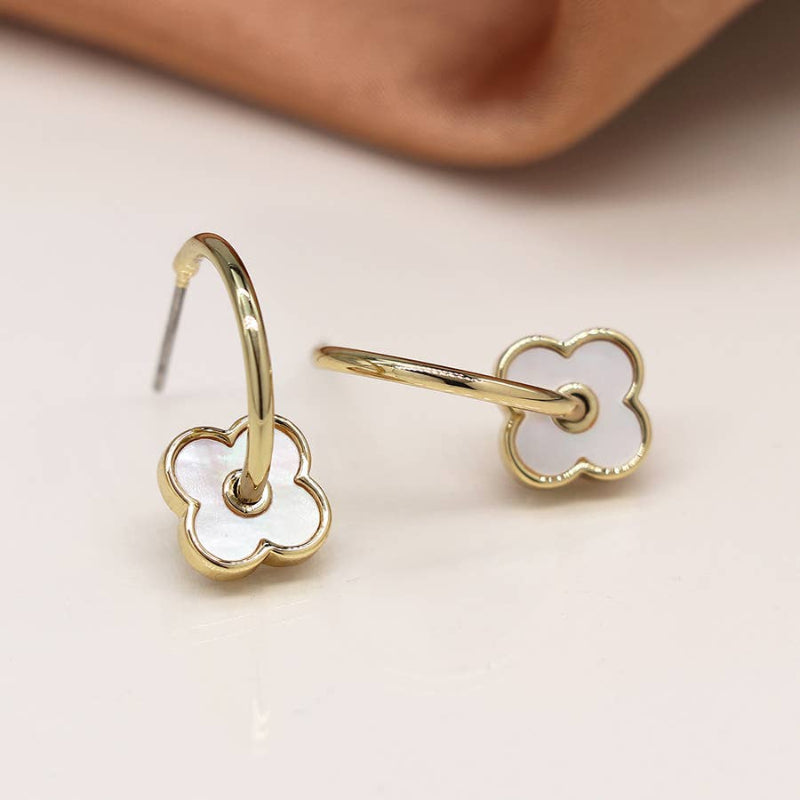 Gold earrings with white floral designs on a beige background
