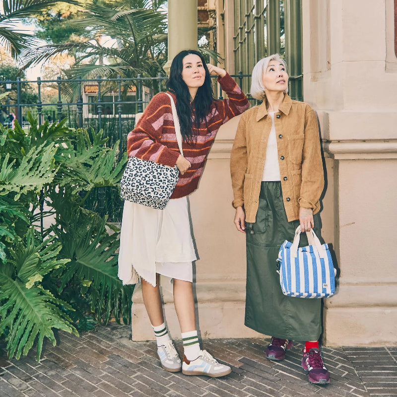 Two people standing outdoors with Roka hampstead lunch bags and a building in the background