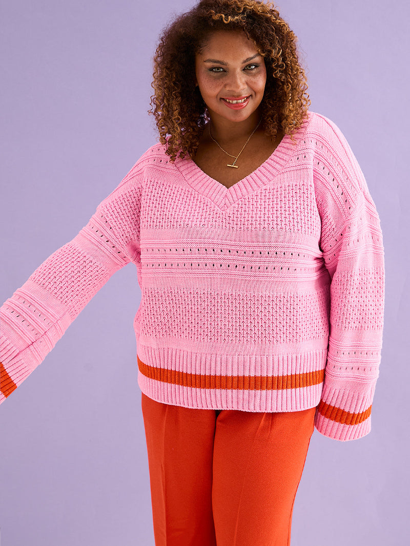 Woman wearing a pink sweater with red trim against a purple background