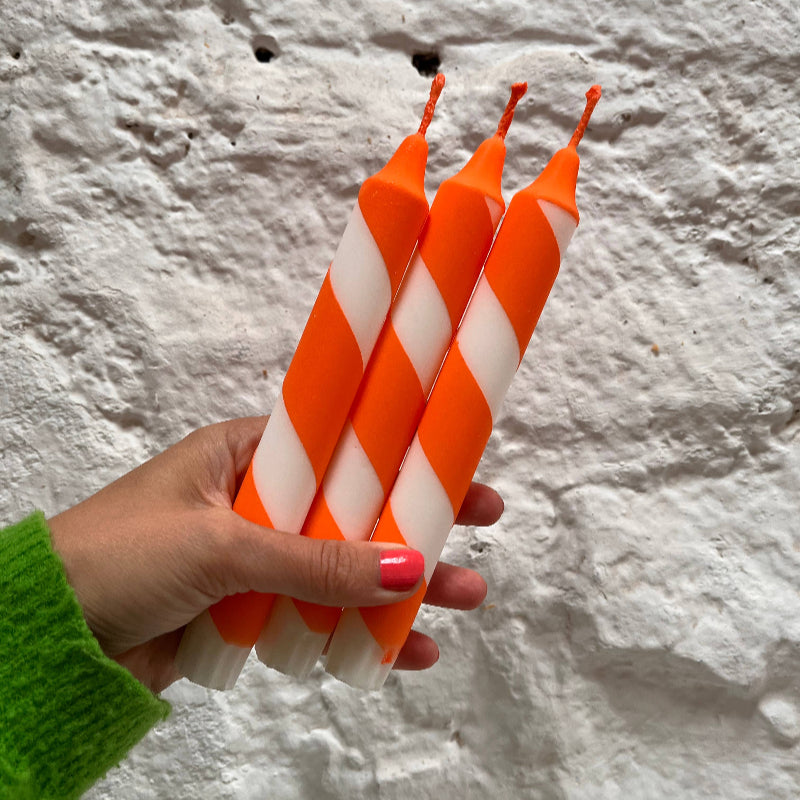 Hand holding three orange and white striped candles against a textured white background