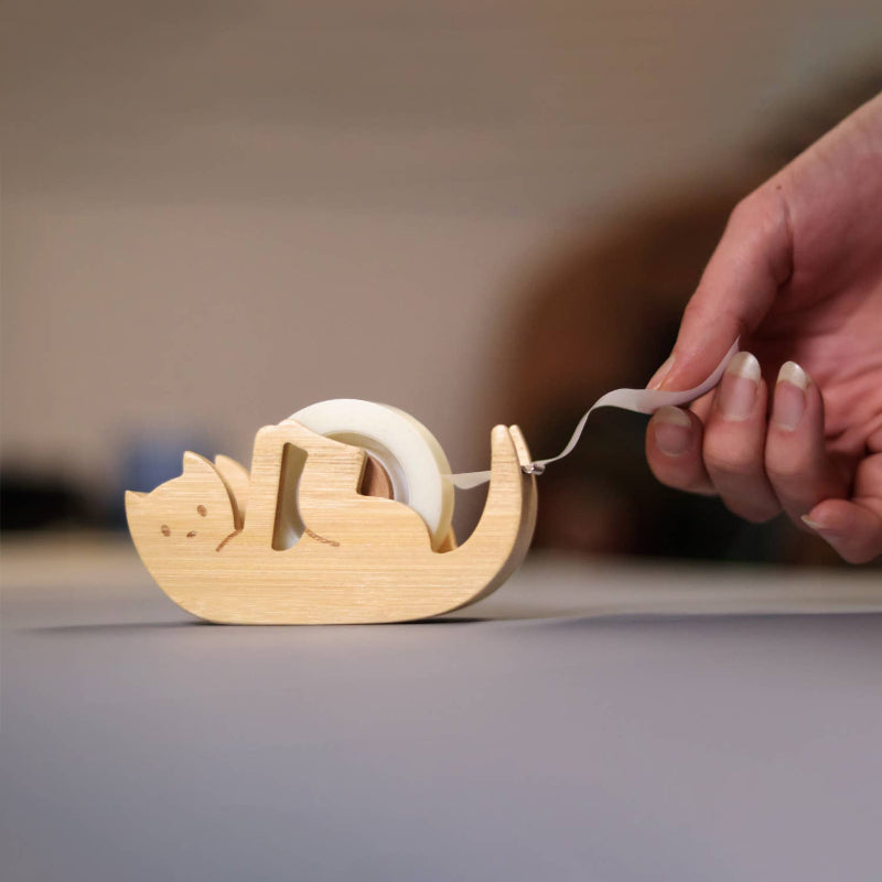 Wooden Kitty Sticky Tape Dispenser with a hand pulling tape from it on a neutral background