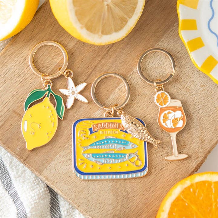 Three keychains with lemon, fish, and cocktail designs on a wooden surface.