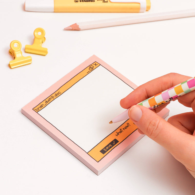 Person writing on a pink memo pad with a colourful pen, surrounded by office supplies on a white background.