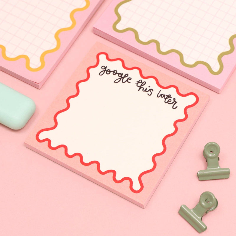 Pink notepad with 'Google this later' text on a pink background with clips and a eraser.